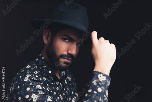 brutal looking bearded Latin American man touching his hat studio shot medium closeup black background . High quality photo
