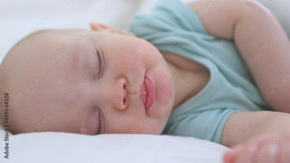 close-up portrait of sleeping infant of three months baby, child lying with closed eyes, moving lips mouth on white bed. little baby kid moving hand in dream, while sleeping. asleep child in bedroom close-up portrait of sleeping infant of three months baby, child lying with closed eyes, moving lips mouth on white bed. little baby kid moving hand in dream, while sleeping. asleep child in bedroom