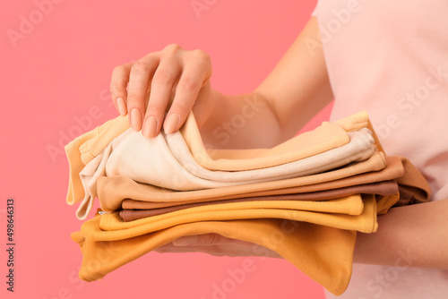 Woman with stack of baby clothes on pink background, closeup