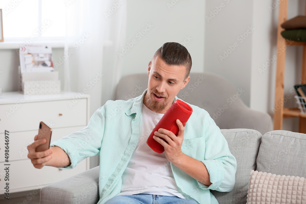 Man taking selfie with wireless portable speaker on sofa in room Man taking selfie with wireless portable speaker on sofa in room