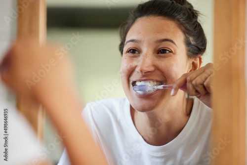 If you want healthy teeth  you have to brush twice a day. Shot of a young woman brushing her teeth while looking into the bathroom mirror.