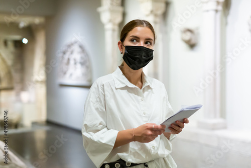 Portrait of young attractive woman in face mask visiting exhibit at sculpture hall in historical museum