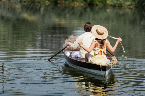 back view of woman in straw hat having boat ride with boyfriend.