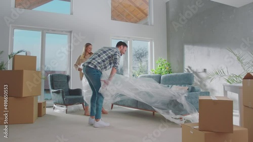 A happy couple removing the cover from their new sofa and sitting on it in slow-motion at their living room photo