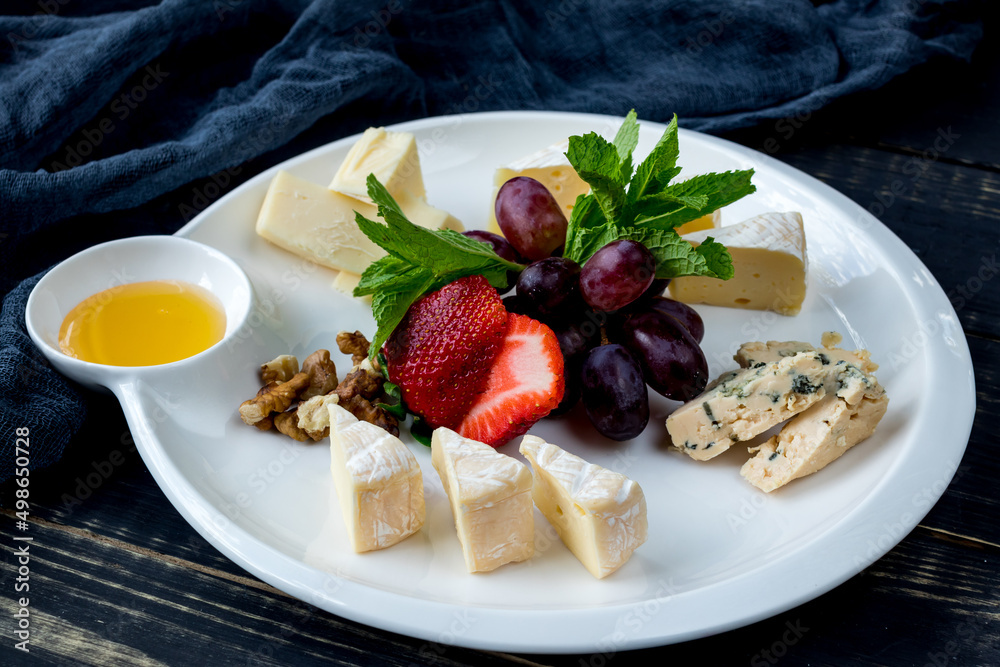 assorted European cheeses on a plate with honey, strawberries, grapes and walnuts with mint assorted European cheeses on a plate with honey, strawberries, grapes and walnuts with mint