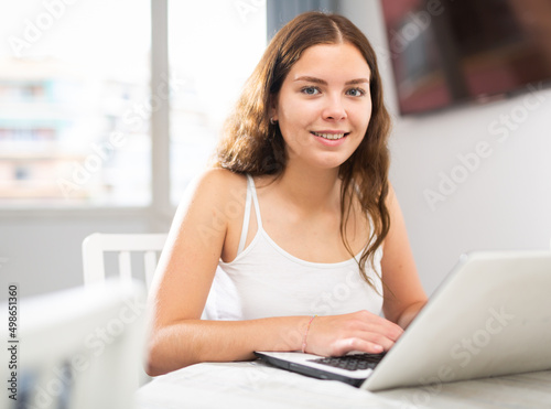 Portrait of positive young woman working on laptop sitting at table in living room Free Download Portrait of positive young woman working on laptop sitting at table in living room - GFXLoad