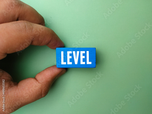 Top view hand holding colored wooden block with text LEVEL on green background.
