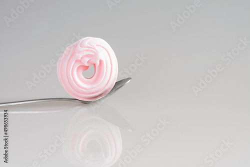 Gray background with pink sugar meringue in a spoon