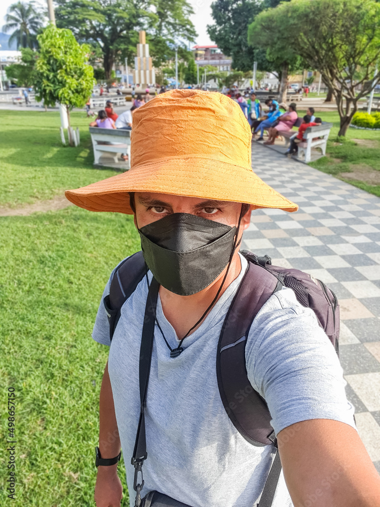 Portrait of a tourist with a medical mask, backpack, and camera taking a selfie with a cell phone