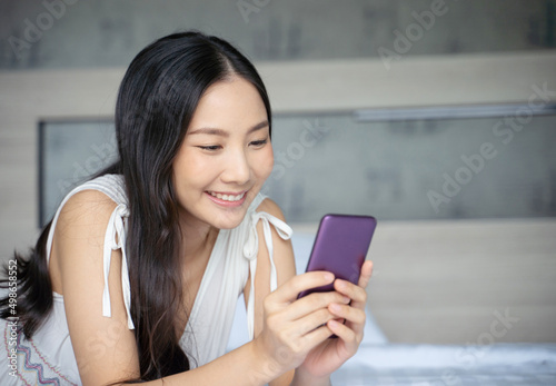 Young Asian woman using smart phone in bedroom happy and smile.