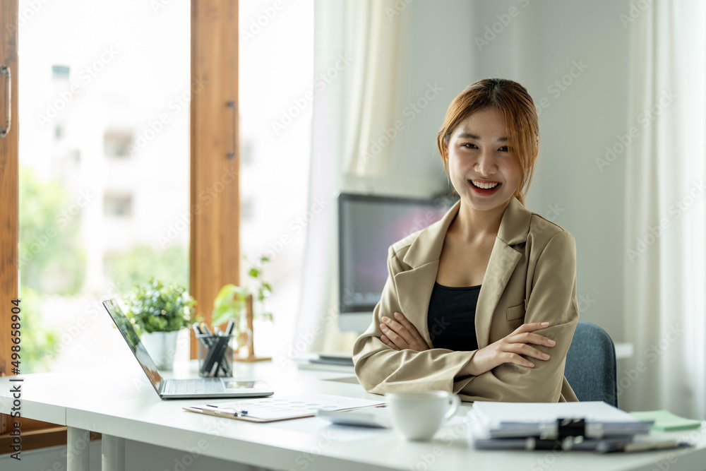 Portrait of young beautiful asian businesswoman looking at camera and smile, arms crossed in modern office workplace