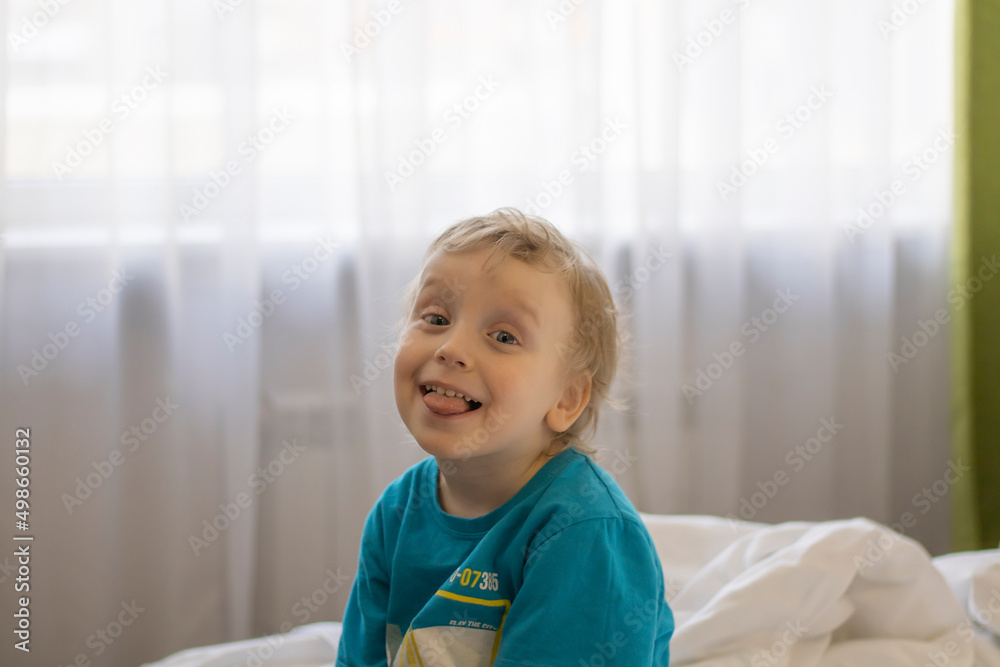 a little boy shows his tongue while sitting on a bed in bright clothes. a little boy shows his tongue while sitting on a bed in bright clothes.