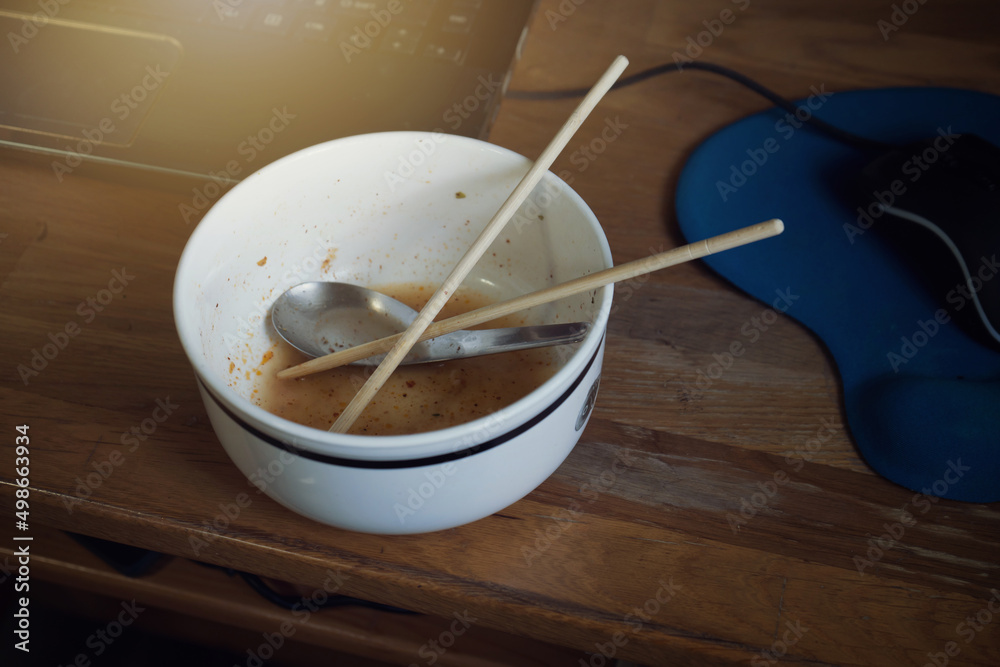 Work from home. Low key image of short spoon and chopsticks in bowl ceramic of finished eating instant noodles after working in front of notebook computer with urgent. Work from home. Low key image of short spoon and chopsticks in bowl ceramic of finished eating instant noodles after working in front of notebook computer with urgent.
