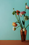 Vertical still life composition of flower bouquet in brown glass vase against light bluish green wall background