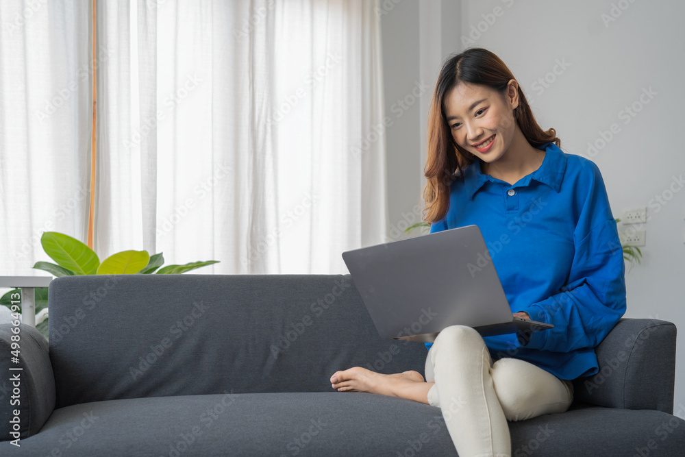 Young business freelance Asian woman working on laptop checking social media while sitting on the sofa when relax in living room at home. Young business freelance Asian woman working on laptop checking social media while sitting on the sofa when relax in living room at home.