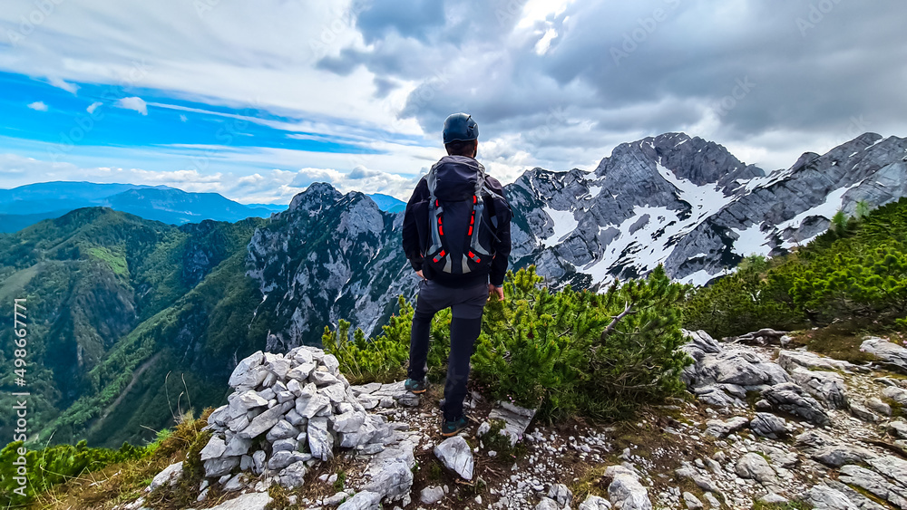 Man with backpack and helmet hiking on path with scenic view on mountains Kamnik Savinja Alps in Carinthia, border Slovenia Austria. Velika Baba, Vellacher Kotschna. Mountaineering. Freedom concept