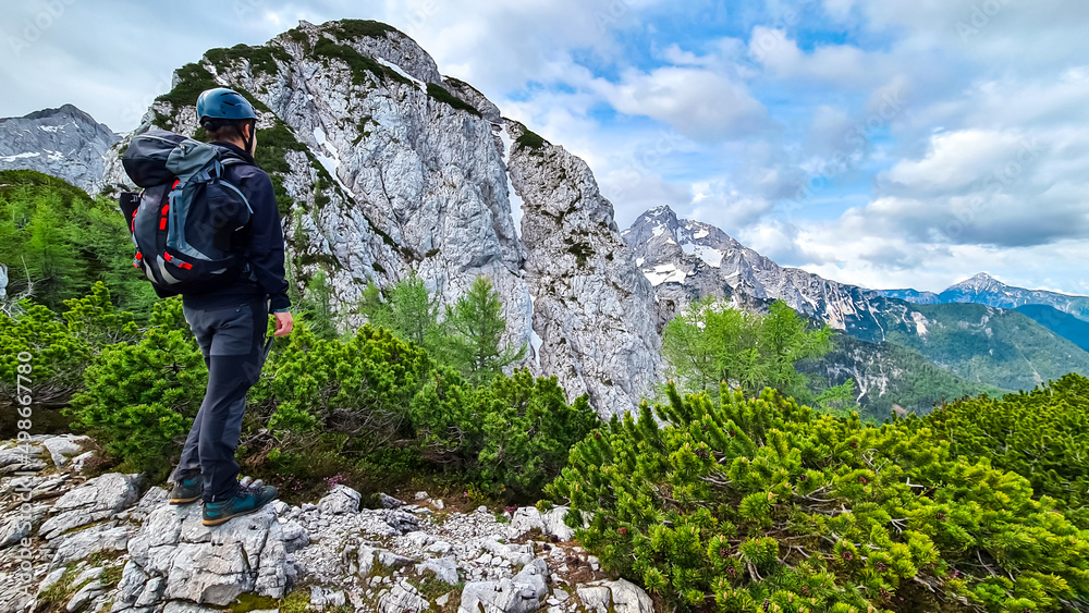 Man with backpack and helmet hiking on path with scenic view on mountains Kamnik Savinja Alps in Carinthia, border Slovenia Austria. Velika Baba, Vellacher Kotschna. Mountaineering. Freedom concept