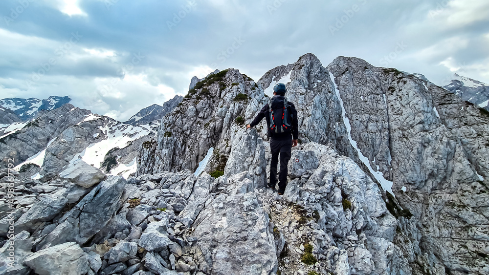 Man with backpack and helmet hiking on path with scenic view on mountains Kamnik Savinja Alps in Carinthia, border Slovenia Austria. Velika Baba, Vellacher Kotschna. Mountaineering. Freedom concept