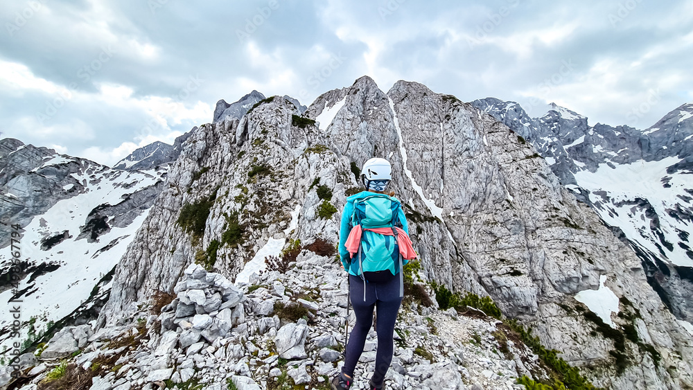 Woman with backpack and helmet hiking on path with scenic view on mountains Kamnik Savinja Alps in Carinthia, border Slovenia Austria. Velika Baba, Vellacher Kotschna. Mountaineering. Freedom concept