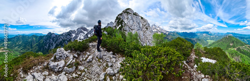 Man with backpack and helmet hiking on path with scenic view on mountains of Kamnik Savinja Alps in Carinthia, border Slovenia Austria. Velika Baba, Vellacher Kotschna. Mountaineering. Freedom concept