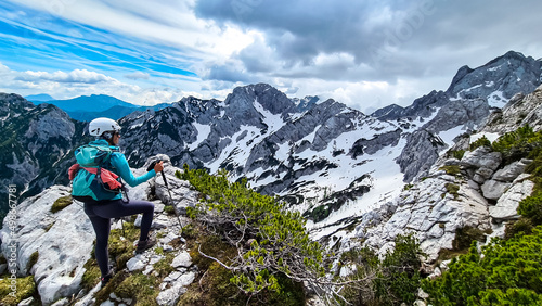 Woman with backpack and helmet hiking on path with scenic view on mountains Kamnik Savinja Alps in Carinthia, border Slovenia Austria. Velika Baba, Vellacher Kotschna. Mountaineering. Freedom concept