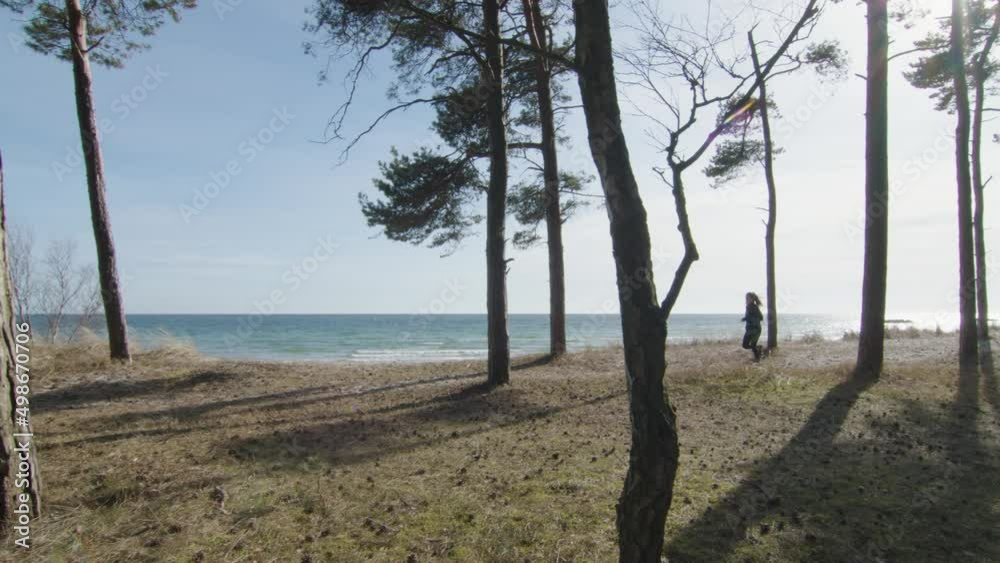 Woman jogging among trees by the beach on a sunny warm day. Running from right to left with tracking pan camera in slow motion. Blue sky green ocean with earth tones in foreground. High Quality Woman jogging among trees by the beach on a sunny warm day. Running from right to left with tracking pan camera in slow motion. Blue sky green ocean with earth tones in foreground. High Quality