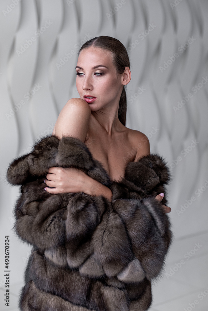 The beautiful woman was wrapped up in fluffy fur of a fur coat is photographed in white studio. Commercial style