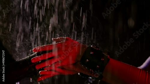 Close-up of female fetishists hands in the rain in neon light. Same-sex relationships