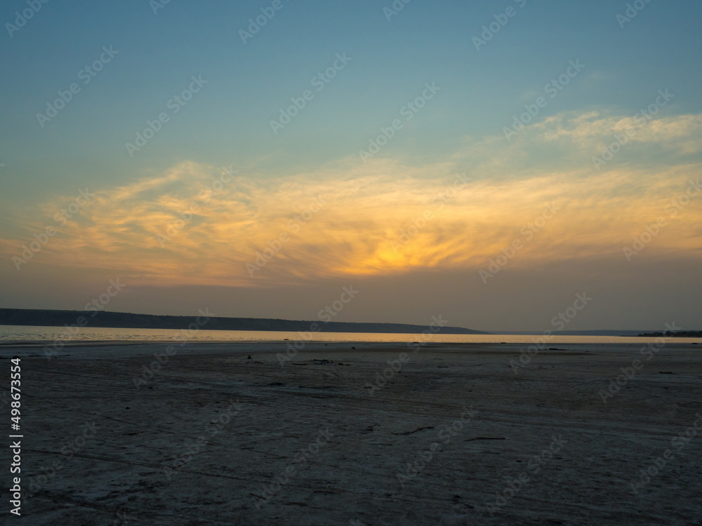 Dried up sandy estuary under the boundless sky. Twilight on the salt lake beach.