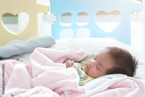 Close up portrait of cute adorable baby girl on white bed in bedroom. Newborn child relaxing sleeping and smiling in the bed in children nursery. Family morning at home.