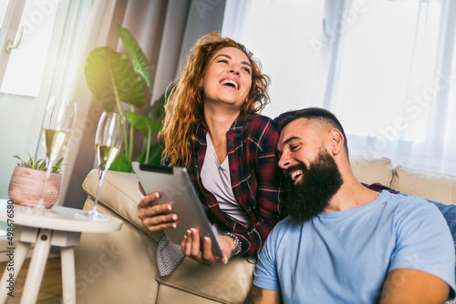 Young couple watching media content online in a tablet sitting on sofa in the living room