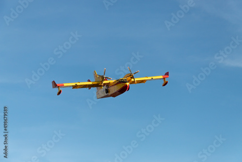 Hydroplane for the extinction of forest fires flying in a deep blue sky. Red and yellow aircraft. Front view. Isolated.