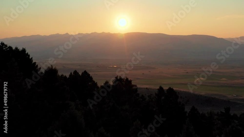 An onward moving aerial shot of trees and a sunset while revealing the Paradise Valley of the Yellowstone River in southwestern Montana. The valley is flanked by the Absaroka Range and Gallatin Range. photo