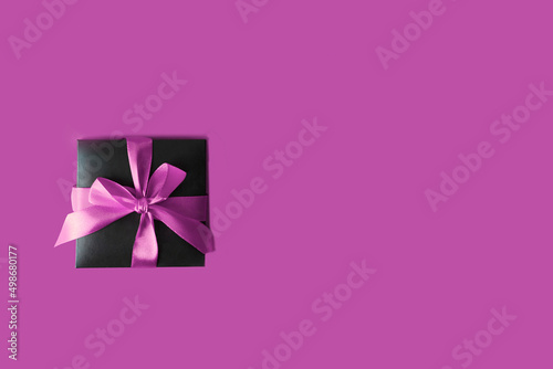 .Black Gift box with violet bow on purple background. Top view and copy space.