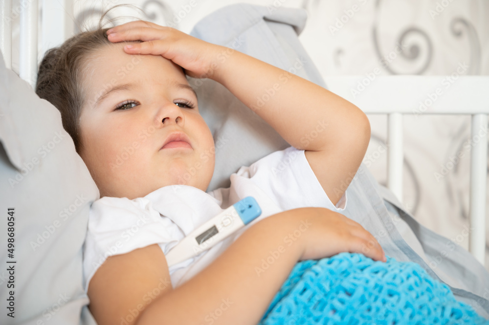 The little boy is sick in bed with a thermometer and high temperature The little boy is sick in bed with a thermometer and high temperature