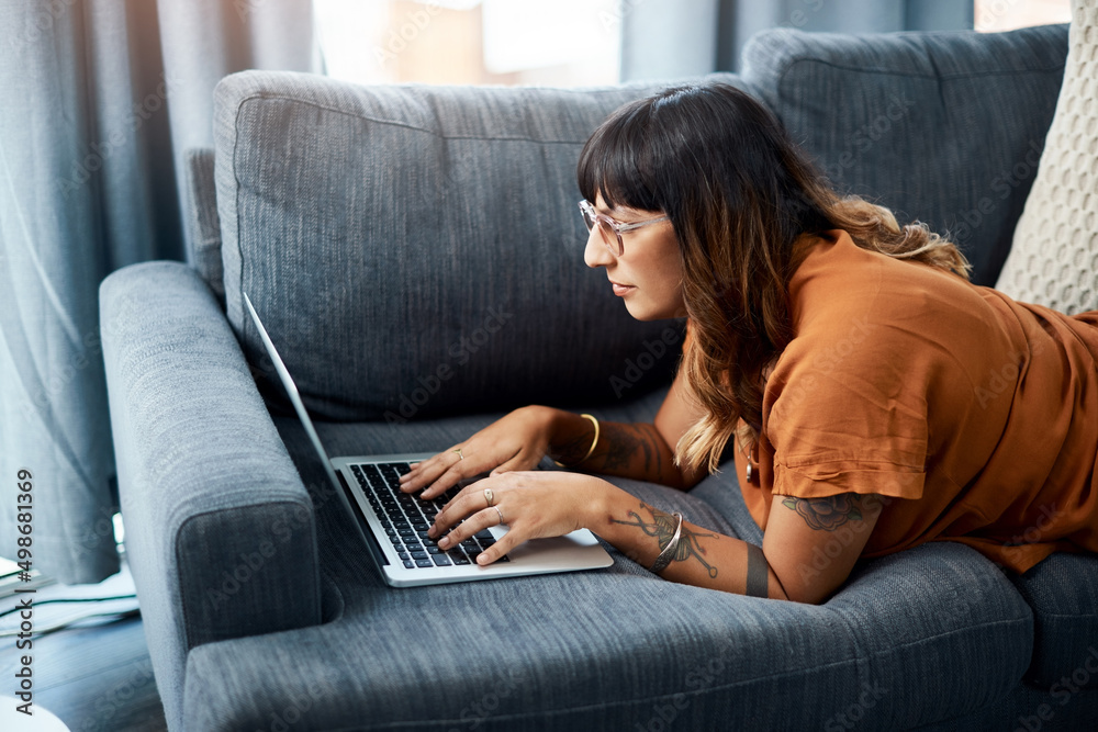 Just browsing to pass time. Shot of a young woman using her laptop while relaxing at home.