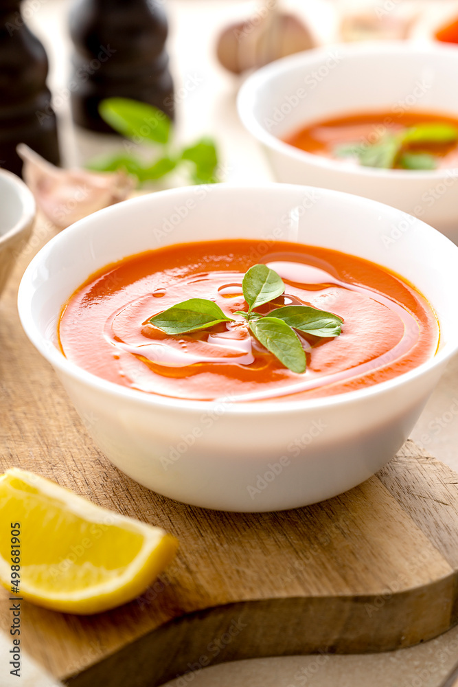 Tomato soup with fresh basil in white bowls. Bright background. Vegan creamy soup. Tomato soup with fresh basil in white bowls. Bright background. Vegan creamy soup.