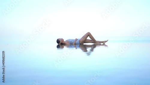 A woman lies on her back in the shallow end of an infinity-edge pool giving the illusion she is floating in midair. Title space photo