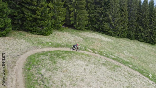 A Young Biker Riding On A Curved Path In Green Hill Landscape At Malino Brdo Resort, Ruzomberok, Liptov, Slovakia. - Drone Tracking Shot photo
