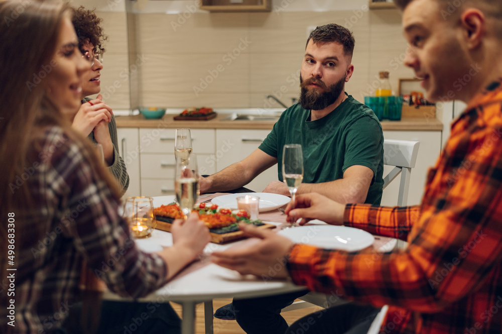 Group of friends enjoying dinner while sitting at the kitchen table together Group of friends enjoying dinner while sitting at the kitchen table together