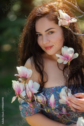 Beautiful girl with flowers of magnolia. Portrait of young smiling brunette woman under blossom magnolia tree.