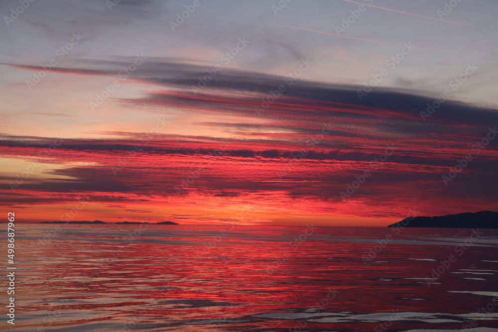 Bright scarlet sky over the sea after sunset over the horizon