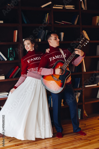 Beautiful couple in red sweaters playing at gitar.
