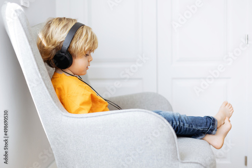 Barefoot boy in headphones watching cartoons on tablet photo