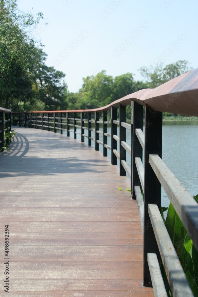 Brown wood walkway and black painted metal fence beside pond in park, Thailand. Brown wood walkway and black painted metal fence beside pond in park, Thailand.