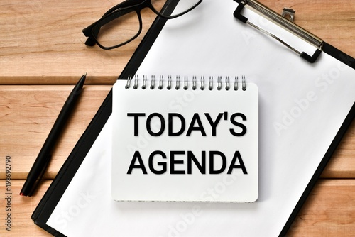 Finance and economics concept.  Notebook with the inscription - Todays Agenda with clipboard, eyeglasses and pen on wooden table. 