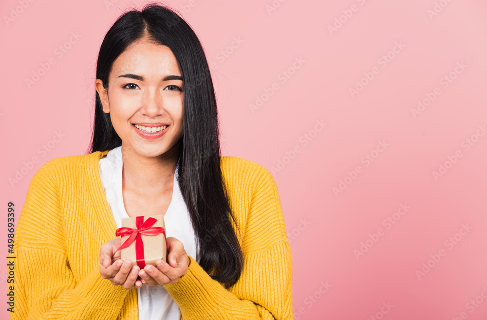 Portrait of happy beautiful Asian young woman smiling holding small gift box on hands, studio shot isolated on pink background, Birthday, New year, Christmas, valentine, holiday day concept Portrait of happy beautiful Asian young woman smiling holding small gift box on hands, studio shot isolated on pink background, Birthday, New year, Christmas, valentine, holiday day concept
