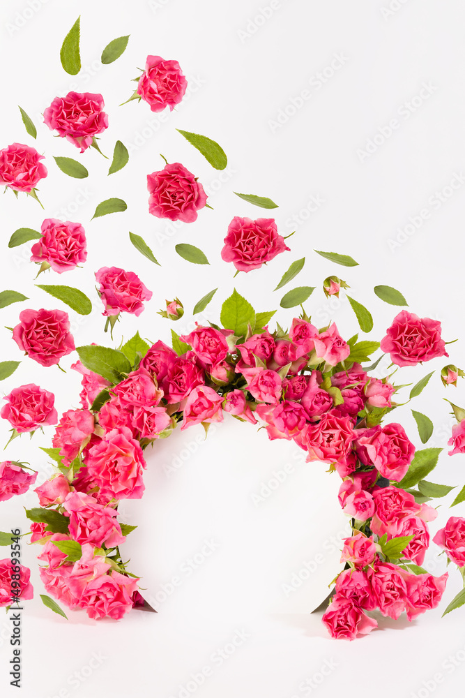 Elegant framing of round arch of fresh little roses as abstract podium with soar buds and green leaves as flow on white stage for presentation cosmetic products, mockup, vertical. Template for design.