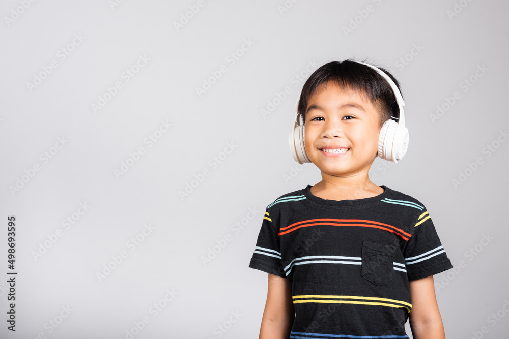 Little cute kid boy 5-6 years old listen music in wireless headphones in studio shot isolated on white background, happy Asian children smiling listening audio, entertainment lifestyle Little cute kid boy 5-6 years old listen music in wireless headphones in studio shot isolated on white background, happy Asian children smiling listening audio, entertainment lifestyle
