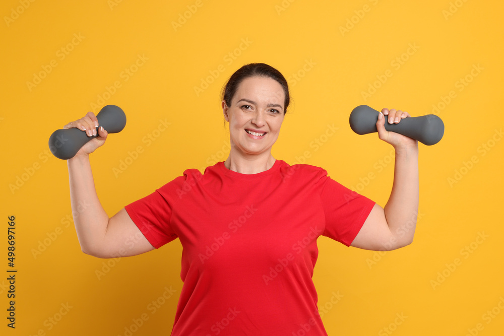Happy overweight woman doing exercise with dumbbells on orange background Happy overweight woman doing exercise with dumbbells on orange background